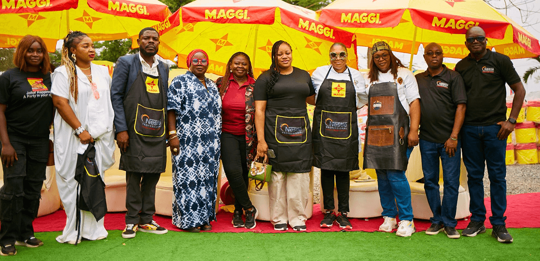 A group of people wearing aprons poses together under bright yellow MAGGI umbrellas at an outdoor event.
