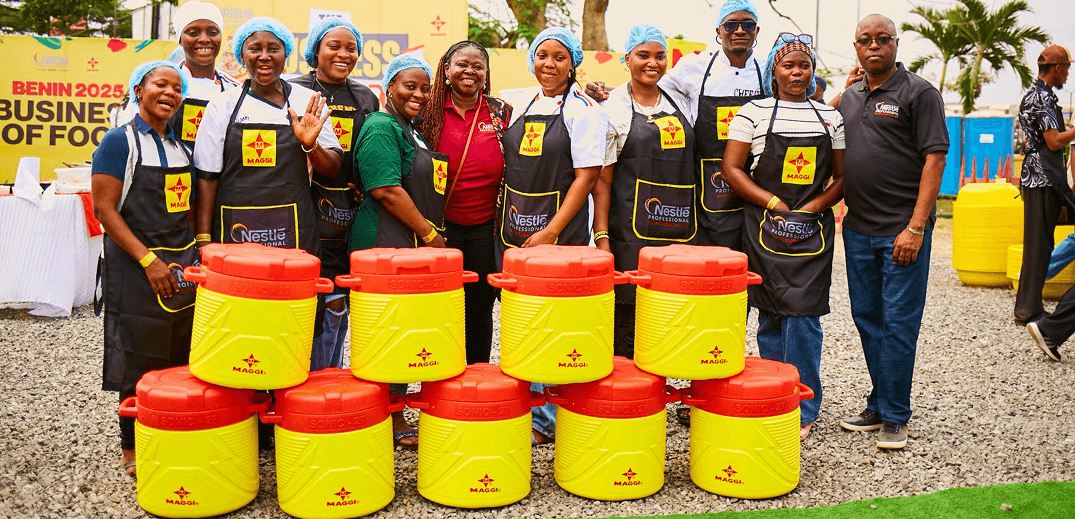 A group of people wearing aprons stands behind a stack of colorful Maggi containers at a culinary event