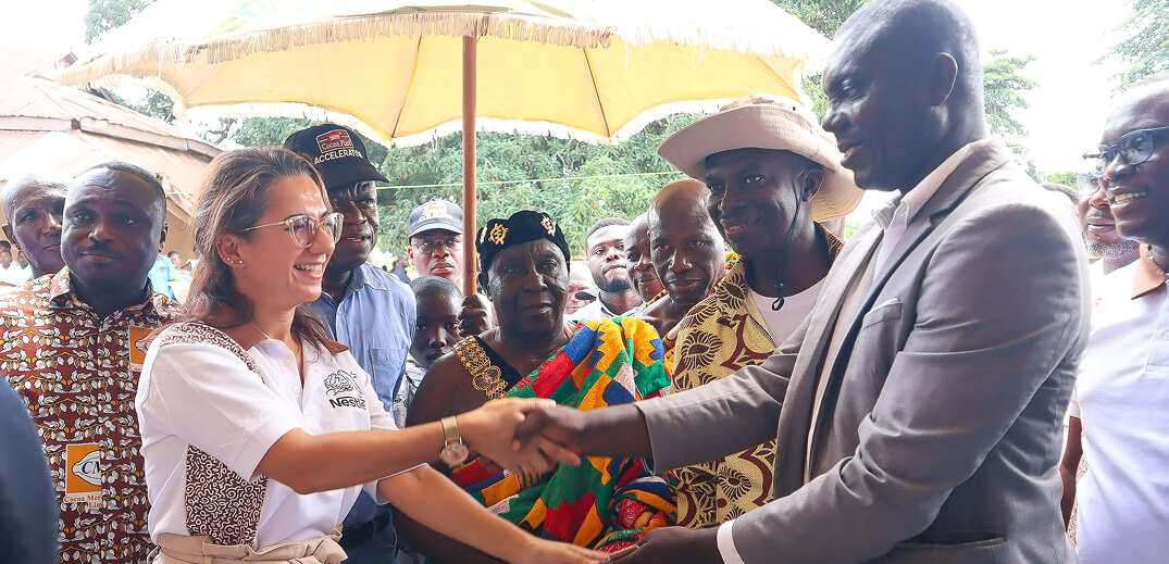A woman in a Nestlé shirt shakes hands with a man, surrounded by a diverse group under a large umbrella.