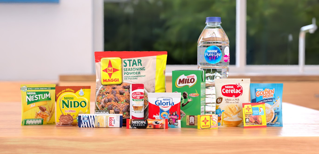 A variety of Nestlé products including cereals, milk, seasonings, and bottled water arranged on a wooden countertop.