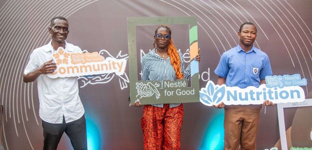 Three people hold Nestlé for Good signs reading "Community," "Nestlé for Good," and "Nutrition" against a curved lined backdr