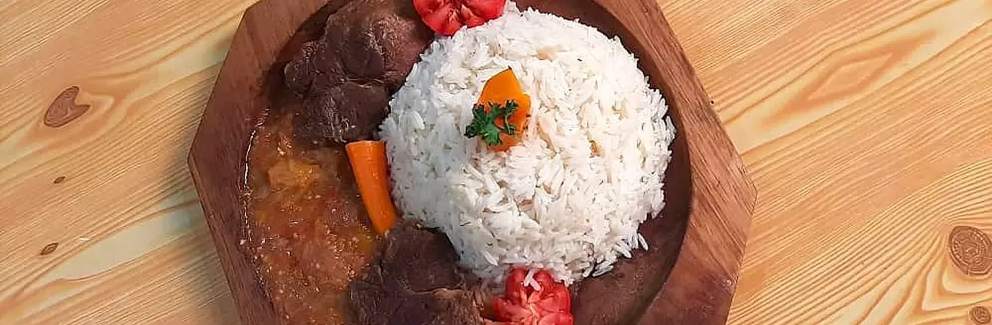 A wooden plate featuring fluffy white rice garnished with parsley, accompanied by tender meat, diced tomatoes, and carrots.