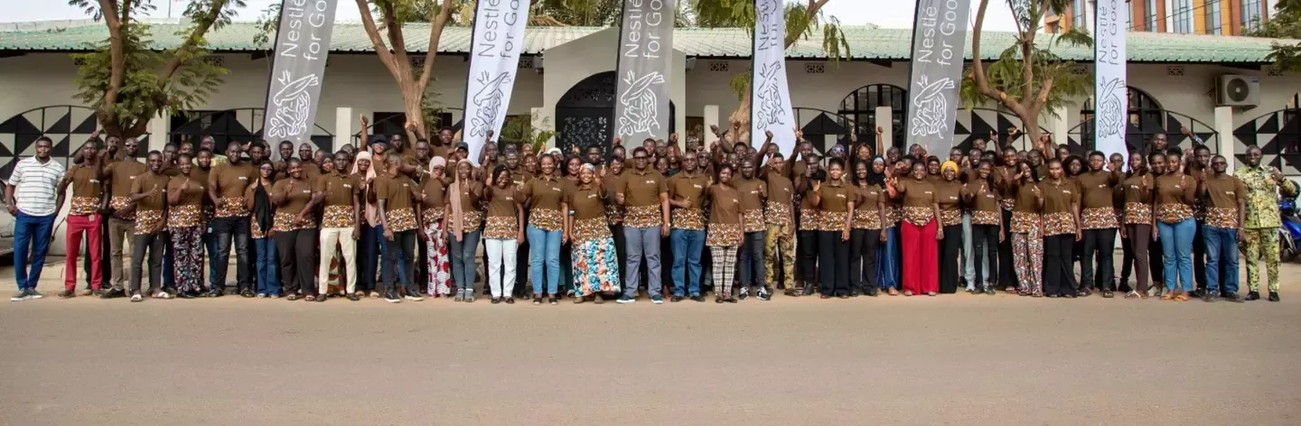 Large group of people standing outdoors in front of a building with Nestlé for Good banners and trees above them.