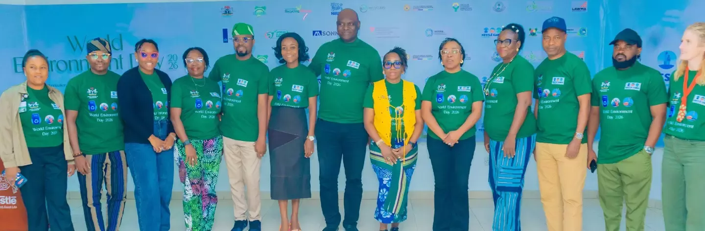 Group of people wearing green World Environment Day 2021 shirts standing indoors in front of a banner.