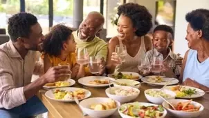 Multigenerational family enjoying a shared meal, smiling and raising glasses around a table filled with food.