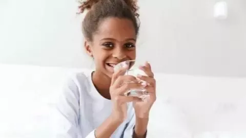 Child drinking water from a glass while sitting with an older adult at home