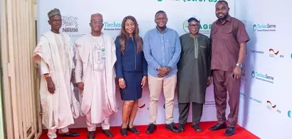 A diverse group of six individuals poses together in front of a branded backdrop featuring logos from Nestlé and TechnoServe.