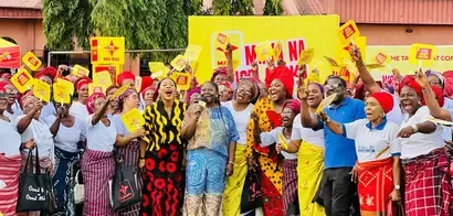 A vibrant group of participants in traditional attire celebrating with yellow signs, gathered in front of a colorful backdrop for a community event