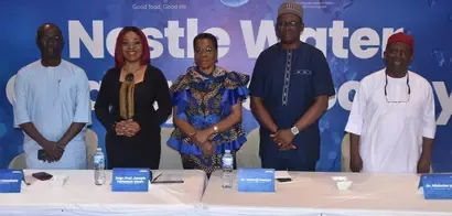 A group of professionals stands at a conference with a Nestlé Water banner in the background, engaging in a formal event