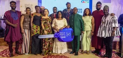 A group of ten people in traditional attire poses together, holding a large blue key labeled "Nestle" at an event celebration.