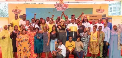 A large group of people stands together, joyfully posing in front of promotional banners for a product giveaway event.