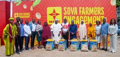 A group of individuals stands in front of a bright, colorful backdrop promoting 'Soya Farmers Engagement,' with farming supplies displayed