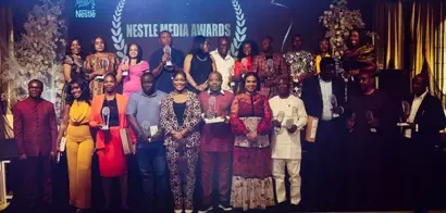 A diverse group of award recipients poses proudly at the Nestle Media Awards, holding trophies against an elegant backdrop