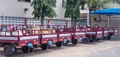 A row of red, utility trucks loaded with goods, marked as donations from Nestlé Ghana Ltd., beside green trees in a courtyard.