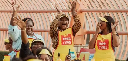 People wearing yellow aprons with "Choisis L'étoile" text raising hands outdoors under a curved metal structure.