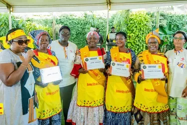 Group of women wearing yellow Maggi aprons and sashes, holding certificates at an outdoor event celebrating Labor Day.