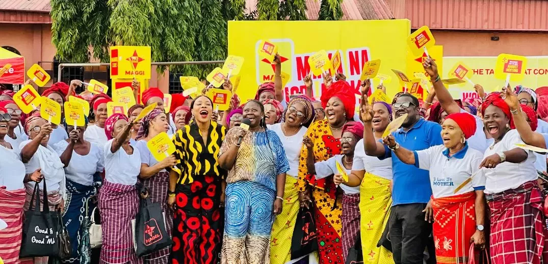 A vibrant group of participants in traditional attire celebrating with yellow signs, gathered in front of a colorful backdrop for a community event
