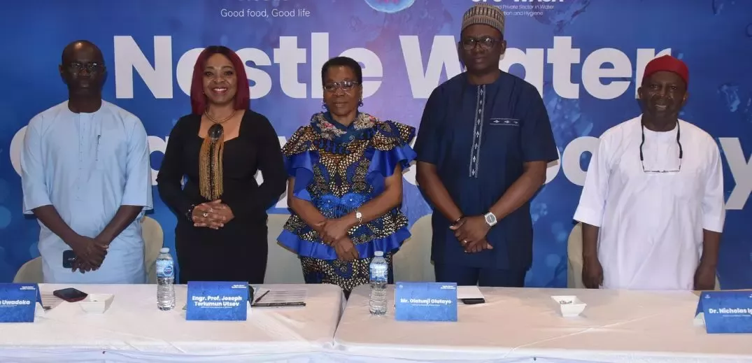 A group of professionals stands at a conference with a Nestlé Water banner in the background, engaging in a formal event
