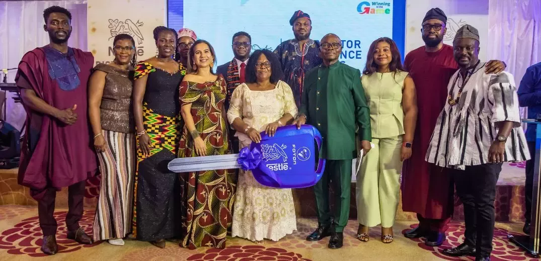 A group of ten people in traditional attire poses together, holding a large blue key labeled "Nestle" at an event celebration.