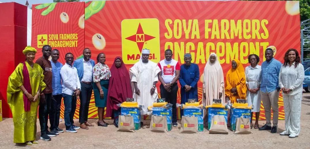A group of individuals stands in front of a bright, colorful backdrop promoting 'Soya Farmers Engagement,' with farming supplies displayed