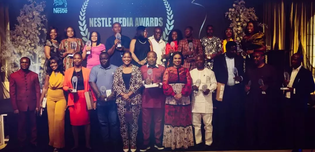 A diverse group of award recipients poses proudly at the Nestle Media Awards, holding trophies against an elegant backdrop