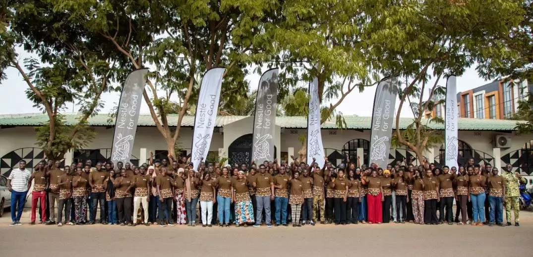 Large group of people standing outdoors in front of a building with Nestlé for Good banners and trees above them.