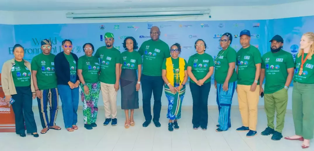 Group of people wearing green World Environment Day 2021 shirts standing indoors in front of a banner.
